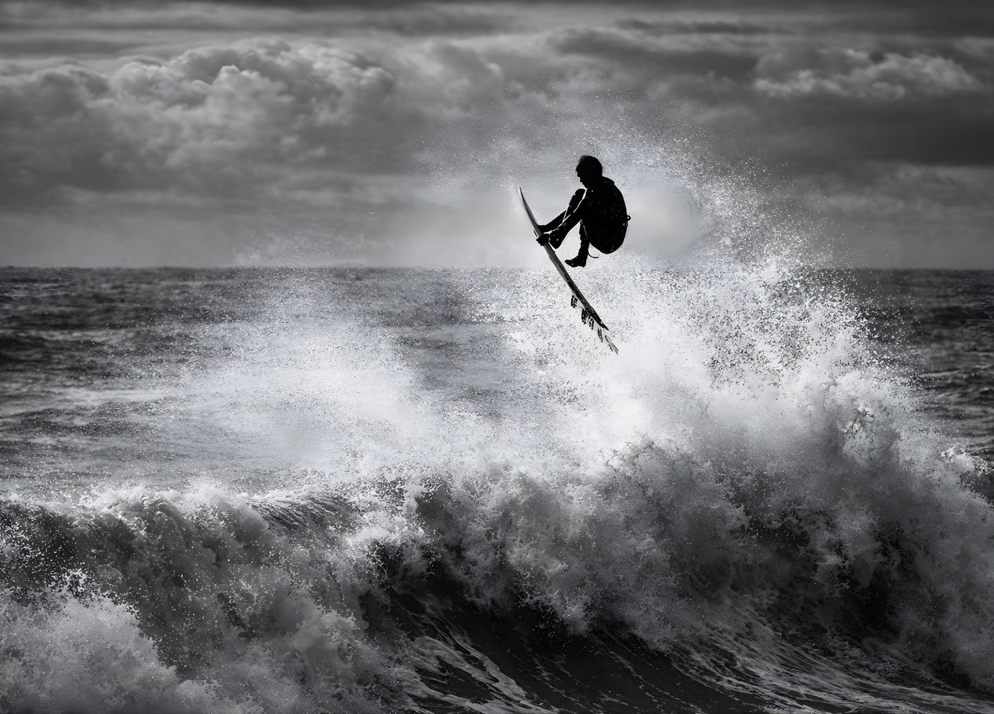 Surfeur en plein saut au-dessus d’une vague photographié en noir et blanc
