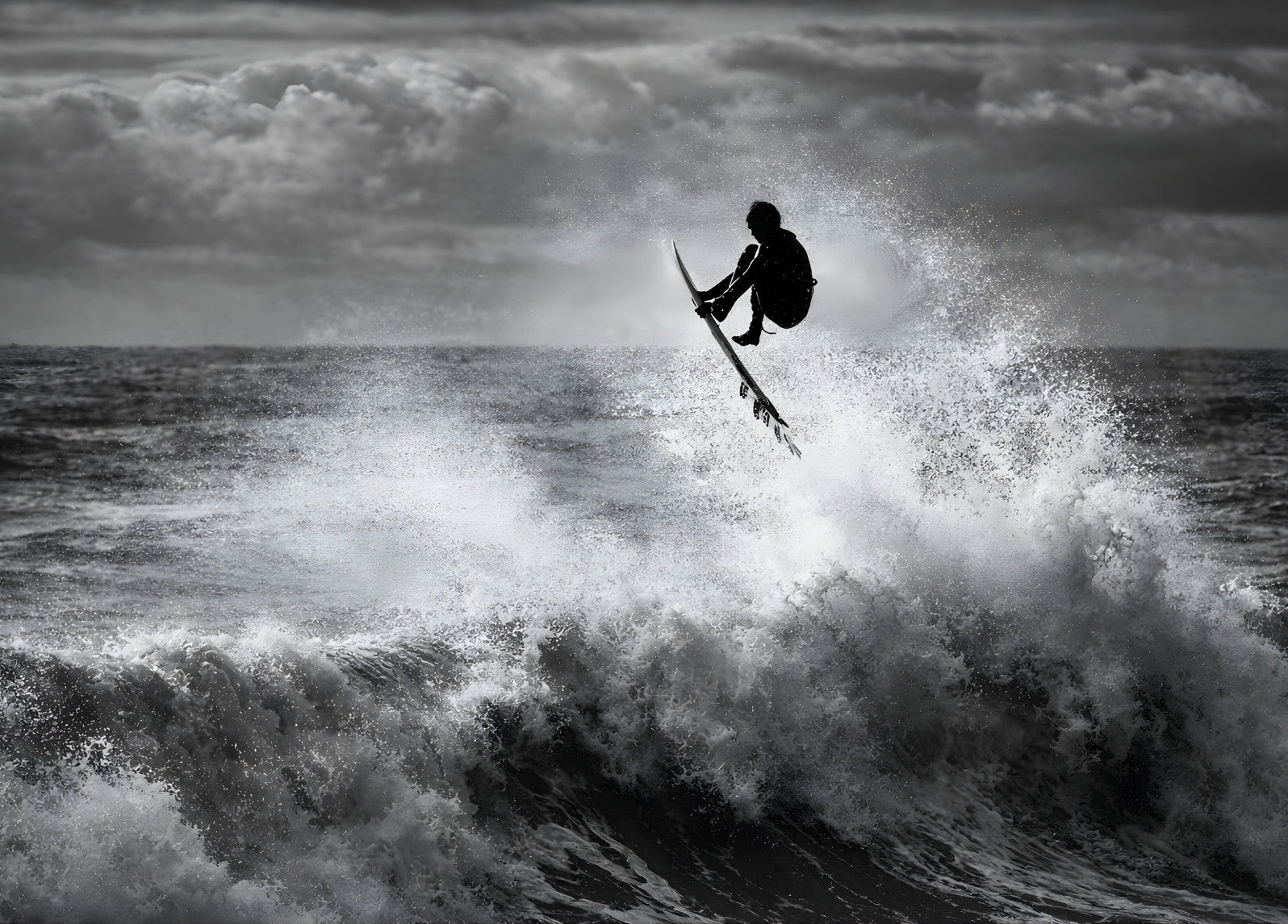 Surfeur en plein saut au-dessus d’une vague photographié en noir et blanc
